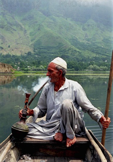INDIA, Kashmir, Srinagar, Nagin Lake. Man sitting in boat smoking a Hookah pipe