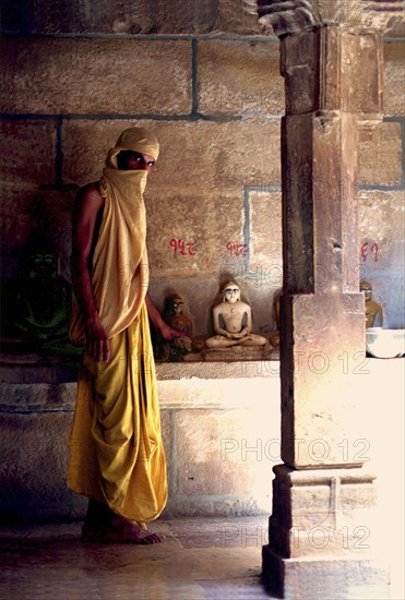 INDIA, Rajasthan, Mt Abu, Fly monk standing near Buddha statues with a scarf covering his head and mouth