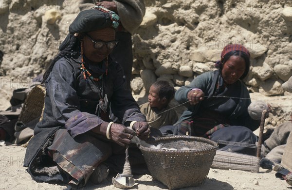 NEPAL, Mustang, Women spinning thread with one wearing head dress displaying turquoise heirloom