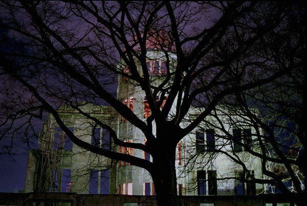 JAPAN, Honshu, Hiroshima, View of the A Bomb Dome illuminated at night seen through silhouetted tree