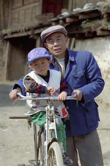 CHINA, Yunnan, Lijiang, Portrait of a man standing with a small boy on his bike holding a Pepsi bottle