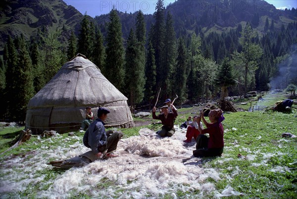 CHINA, Xinjiang, Tianchi, Heavenly Lake. Family outside yurt sitting around mass of fleece