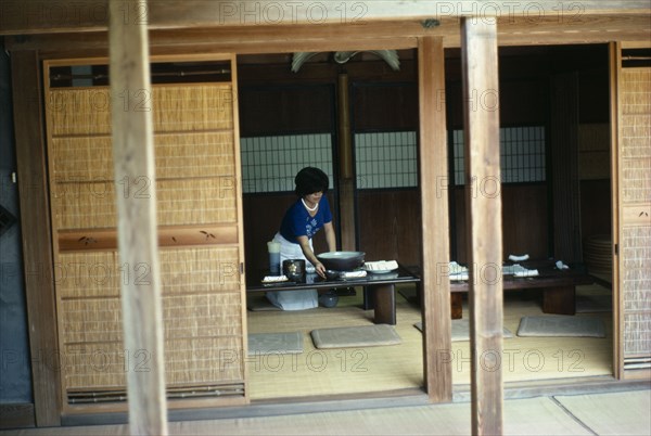 JAPAN, Kagoshima, Satsuma, Home of the potter Chinjukau with moveable wooden screens open to reveal interior with woman laying table.
