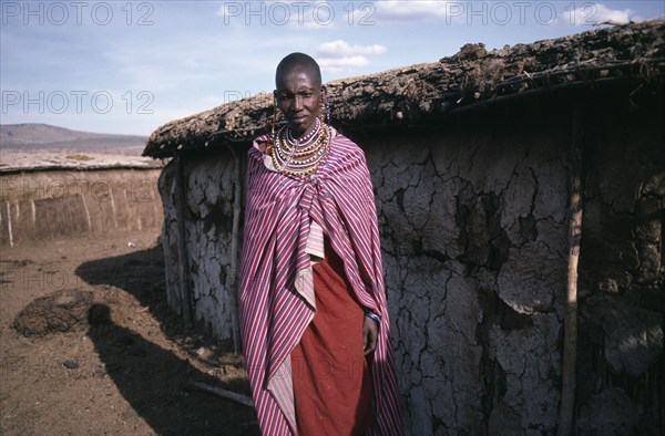 KENYA, Tribal People, Masai woman standing outside traditional mud dwelling near the Masai Mara.