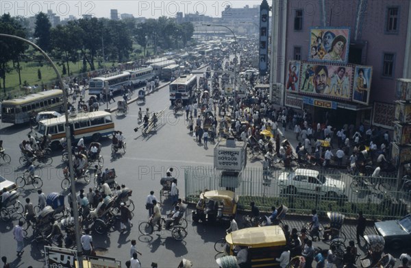 BANGLADESH, Dhaka, Busy street scene with crowds of pedestrians trishaws and buses.  Cinema with billboard advertising films on right.