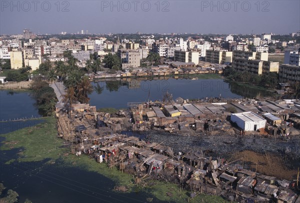 BANGLADESH, Dhaka, Waterside slum dwellings after fire with city buildings beyond.