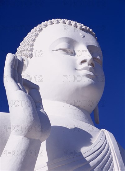SRI LANKA, Mihintale, Large white seated Buddha. Angled detail of head and raised hand.