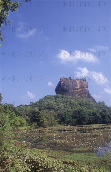 SRI LANKA, Sigiriya, View towards huge monolithic rock site of fith century citadel. Also called Lion Rock. Lake with water lillies in foreground.