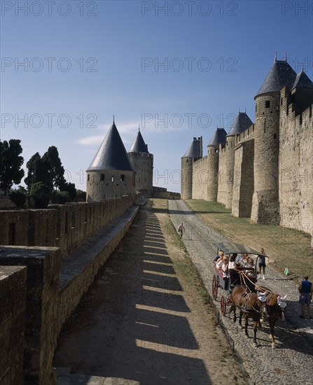 FRANCE, Languedoc Roussillon, Aude, Carcassone. La Cite inner and outer ramparts with hourse drawn carriage transporting tourists along cobbled path in between