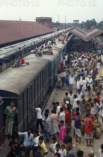 BANGLADESH, Bramanbahria, Train loaded with passengers in station with crowds on the platform and people sitting on the train roof.