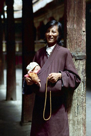 CHINA, Tibet, Lhasa, Portrait of father with small child tucked in his clothing outside the Jokhang Temple