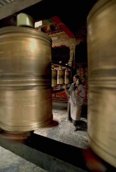 CHINA, Tibet, Lhasa, Jokhang Temple. Worshipper walking clockwise spinning prayer wheels with offerings of prayers for the benefit of mankind.