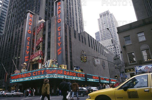 USA, New York, New York, City street scene with Radio City advertising Christmas lineup and yellow cab in the foreground