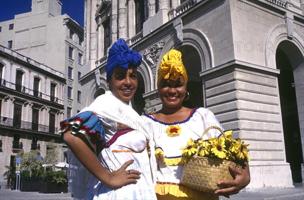 CUBA, Havana, Two smiling women wearing brightly coloured head scarfs standing in the square holding a basket of flowers