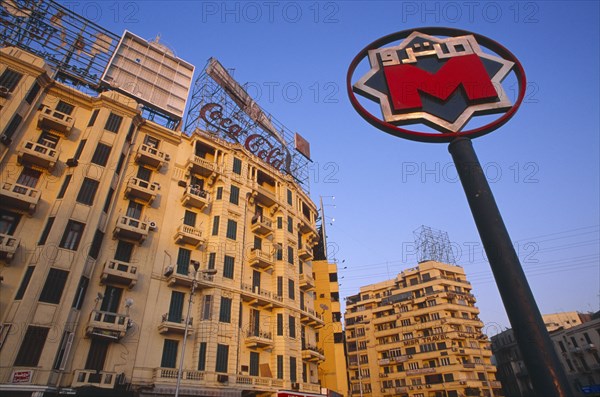 EGYPT, Cairo , Sadat metro station sign on Midan Tahrir with city buildings and advertising for Coca Cola and Kentucky Fried Chicken behind.