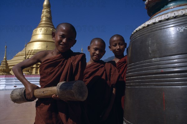 MYANMAR, Thachilek, Young Burmese novice monks at Wat Phra That wao with golden stupa behind.