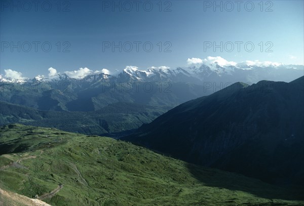 GEORGIA, Caucusas Mountains, Mountain landscape with distant snow covered peaks and dense forest on lower slopes.