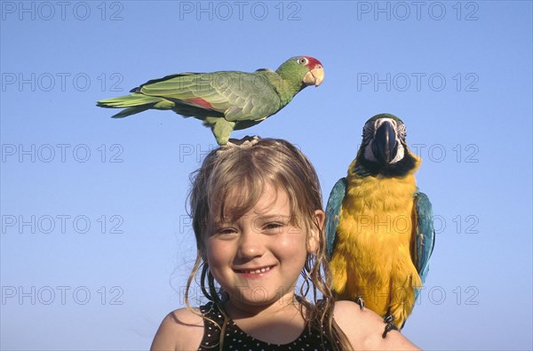 USA, Florida, Fort Lauderdale, Portrait of a young girl with yellow and blue Parrot on her shoulder and a green and red Paroquet on her head
