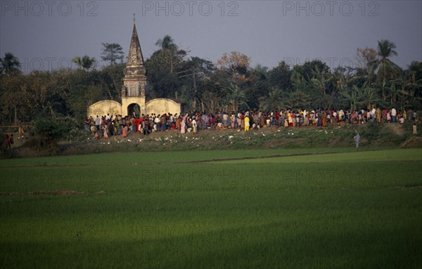 BANGLADESH, Aricha, View over rice fields towards crowds gathered around old Hindu temple at sunset.