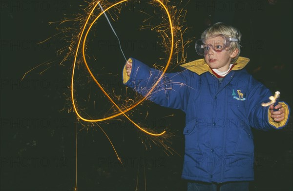 ENGLAND, Oxfordshire, Festivals, Young boy wearing protective eye glasses making circular light trails with sparkler on Guy Fawkes Night