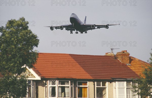 ENGLAND, London, Heathrow, Boeing 747 jumbo jet long haul airliner of British Airways low in flight over rooftops of residential area.