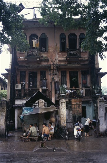 VIETNAM, North, Hanoi, Decayed French colonial style residential buildings with people sheltering from the rain on the pavement