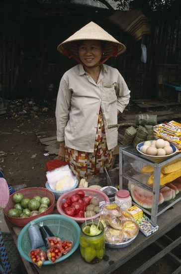 VIETNAM, South, Saigon, Smiling woman wearing traditional conical hat selling fruit and vegetables beside the road