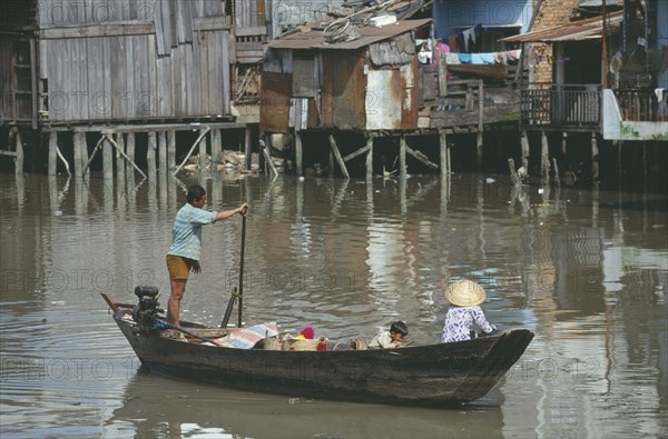 VIETNAM, South, Saigon, Man rowing boat past waterside houses on the Kinh Ben Nghe a tributary of the Saigon River