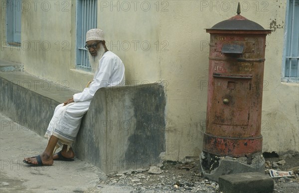 TANZANIA, Zanzibar Island, Elderly Muslim man sitting at roadside beside post box.