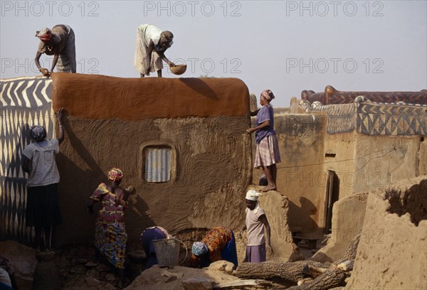 BURKINA FASO, Tiebele, Group of women preparing house front for decorative painting in traditional Gourounsi village.