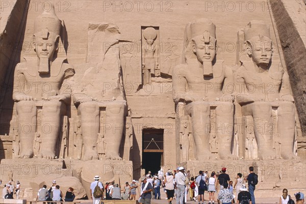 EGYPT, Nile Valley, Abu Simbel, Sun Temple of Ramses II. Tourists at entrance flanked by four colossi of Ramses II.