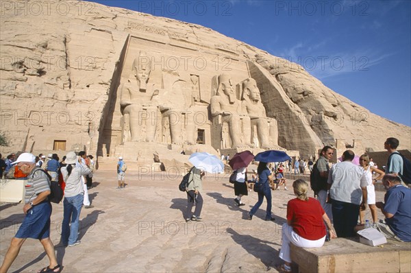 EGYPT, Nile Valley, Abu Simbel, Sun Temple of Ramses II.  Tourists outside entrance flanked by four colossi of Ramses II.