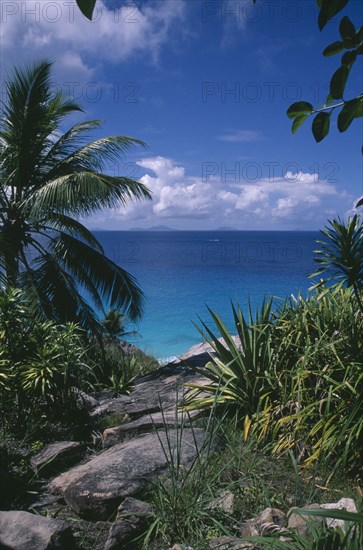 SEYCHELLES, Fregate Island, View through rocks and foliage toward the turquoise sea with islands of Praslin and La Digue on the horizon