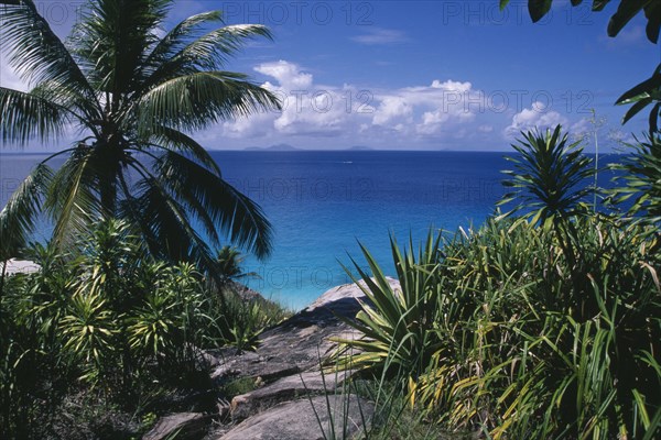SEYCHELLES, Fregate Island, View through rocks and foliage toward the turquoise sea with islands of Praslin and La Digue on the horizon