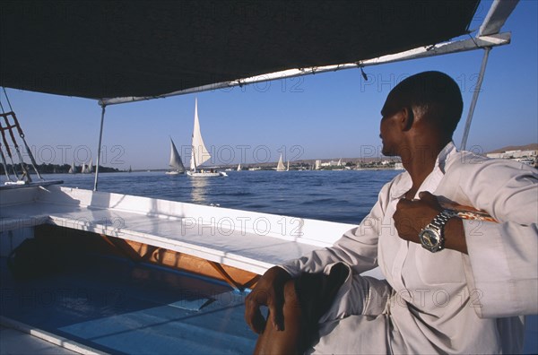 EGYPT, Nile Valley, Aswan, Cropped view of man on board felucca looking across water towards others.