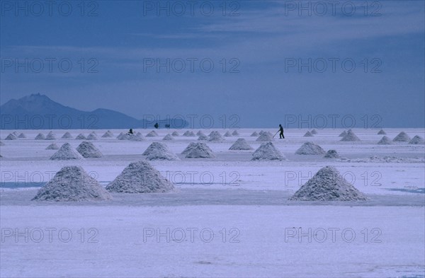 BOLIVIA, Altiplano, Salar de Uyuni, View over the salt plains with figure sweeping up piles of salt for extraction