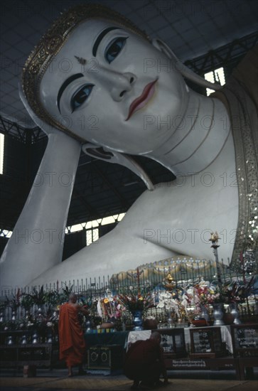 MYANMAR, Yangon, Large reclining Buddha with monks in front of altar in foreground.