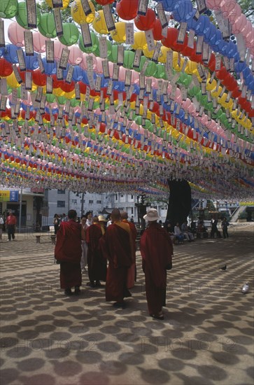 SOUTH KOREA, Seoul, Jogyesa Temple.  Canopy of paper lanterns and prayer streamers hung to celebrate the birthday of Buddha with group of Tibetan Buddhist monks standing below.
