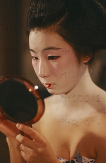 JAPAN, Kyoto, Portrait of a trainee Geisha girl looking in a hand held mirror