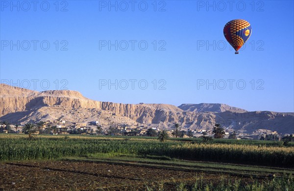 EGYPT, Nile Valley, Thebes, "Valley of the Kings with hot air balloon above agricultural land, village and limestone hills with distant tombs.  "