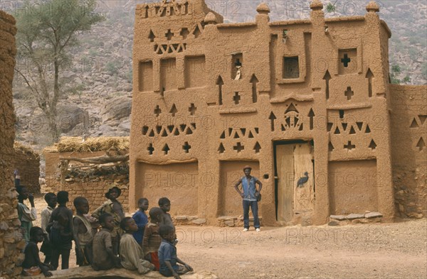 MALI, Architecture, Dogon village Elders house with man standing outside and group of children in the foreground.