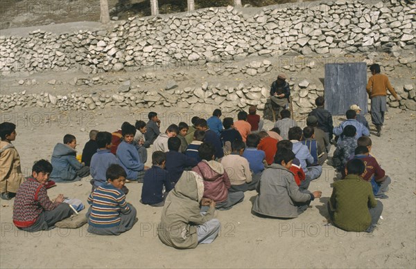 PAKISTAN, North West Frontier, Karimabad, Outdoor classroom for boys only with teacher seated beside blackboard.