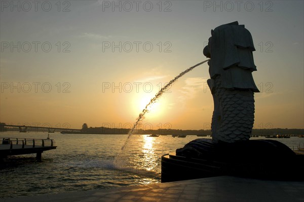 SINGAPORE, Merlion, Merlion statue spouting water in silhouette overlooking Singapore River at sunset