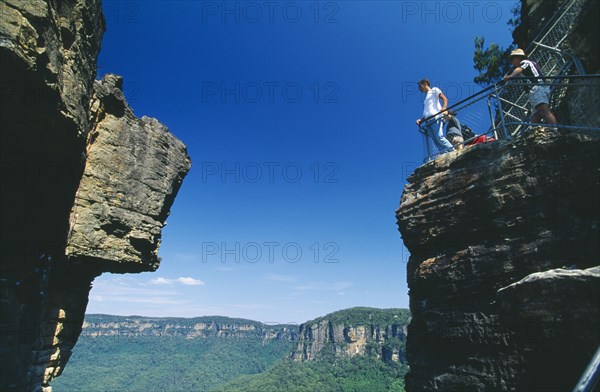 AUSTRALIA, New South Wales, Blue Mountains, View looking up through gap between the Three Sisters cliffs at Katoomba with tourists standing overlooking the edge