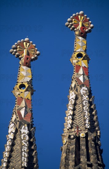 SPAIN, Catalonia, Barcelona, La Sagrada Familia unfinished church designed by Gaudi.  Detail of two spires topped with Venetian mosaic.