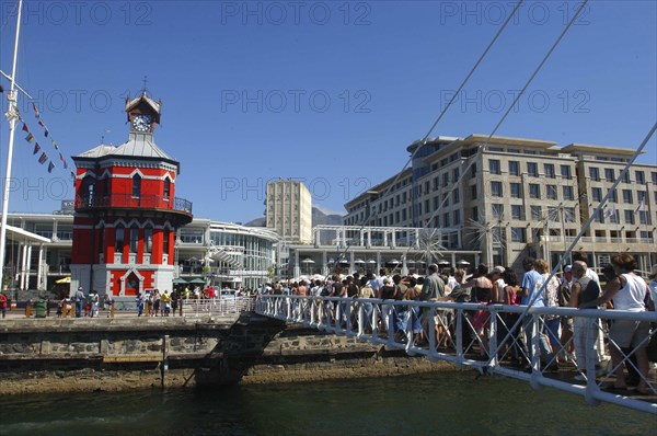 SOUTH AFRICA, Western Cape, Cape Town, Waterfront with queue of people on a bridge crossing over to the brightly coloured clock tower