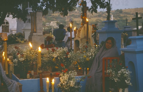 MEXICO, Puebla, Acatlan, Woman keeping vigil beside grave decorated with candles and flowers during Night of the Dead