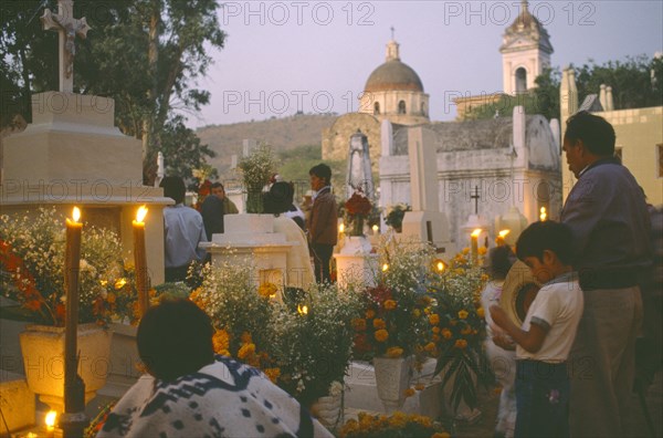 MEXICO, Puebla, Acatlan, People keeping vigil beside graves decorated with candles and flowers during Night of the Dead