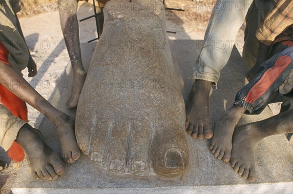 BURKINA FASO, Ougadougou, Boys playing in Managa Sculpture park on the outskirts of Ouga.  Cropped view of their feet as they stand beside the huge stone foot of a sculpture.