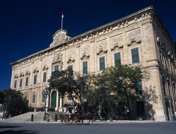 MALTA, Valletta, Auberge de Castille et Leon. Decorative baroque facade  with green doorway and shutters. Horse and carriage travelling past. Maltese flag flying from roof. Official residence of the Prime Minister